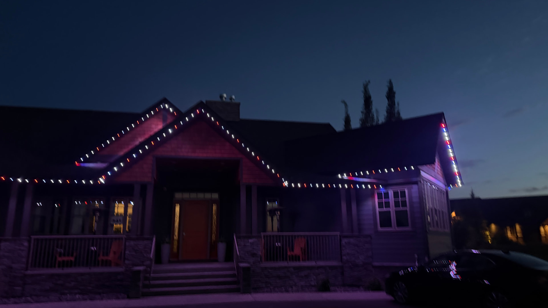 Craftsman-style bungalow at dusk with permanent lights along the porch roofline and gable peaks set to an alternating red, white and blue scene.